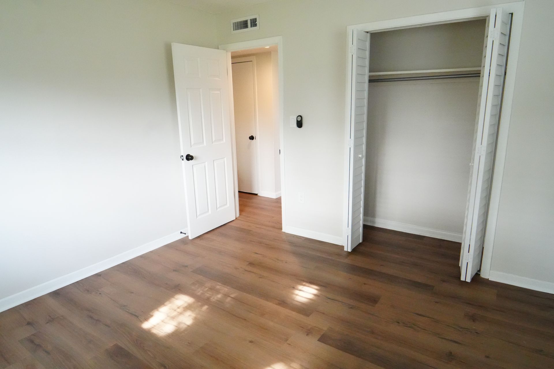 An empty bedroom with hardwood floors and a closet.