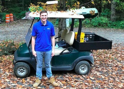 a man in a blue shirt is standing next to a golf cart .