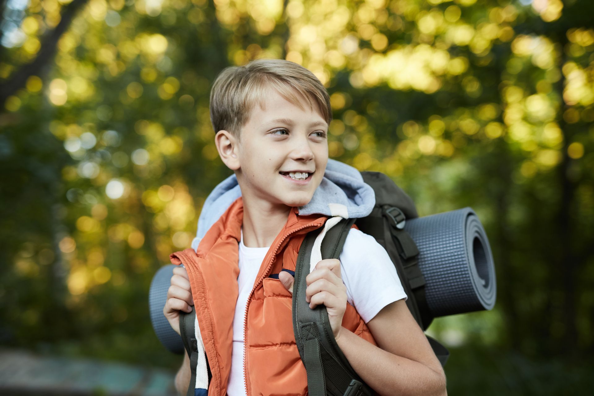 A young boy is carrying a backpack and a yoga mat.