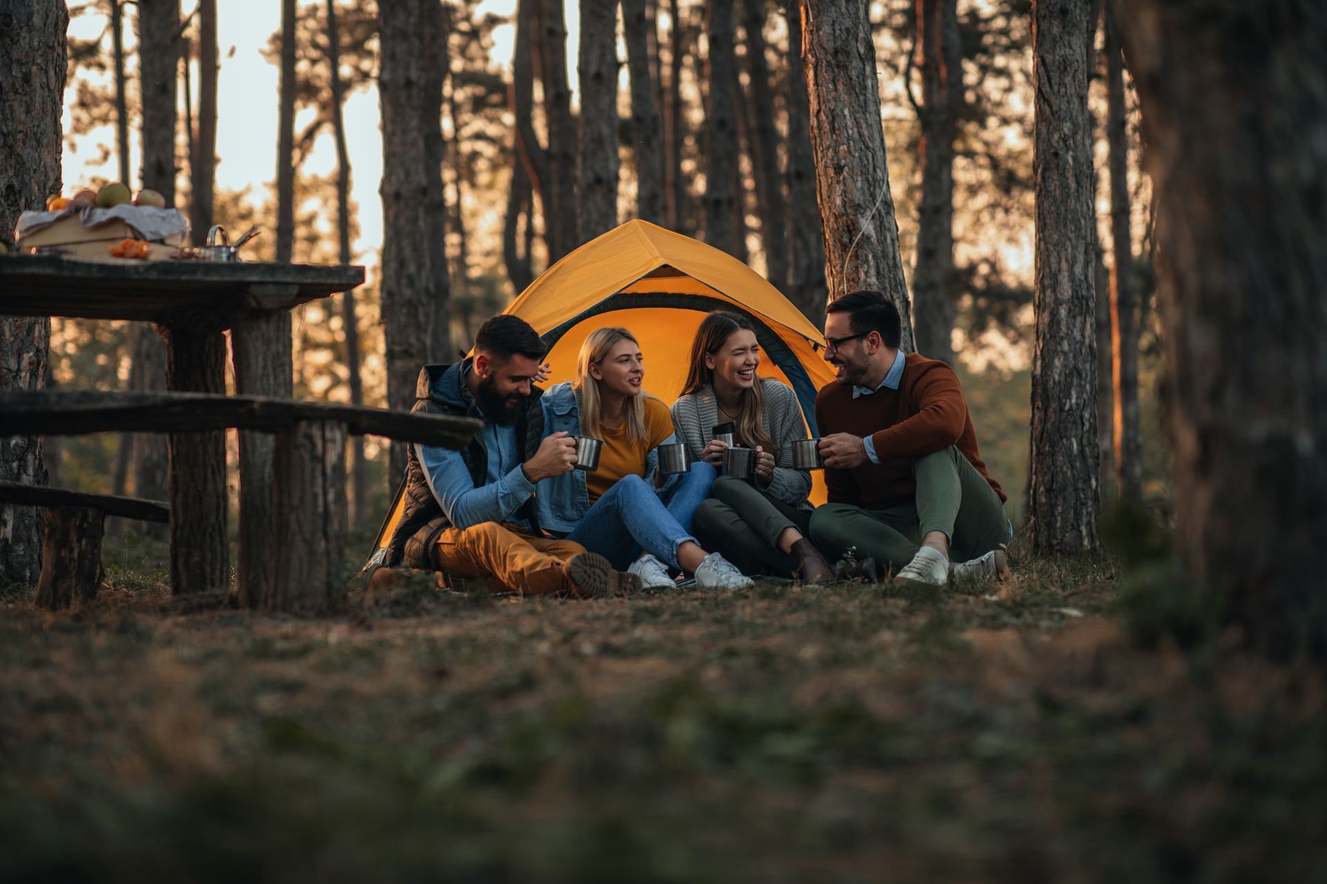 A group of people are sitting in front of a tent in the woods.