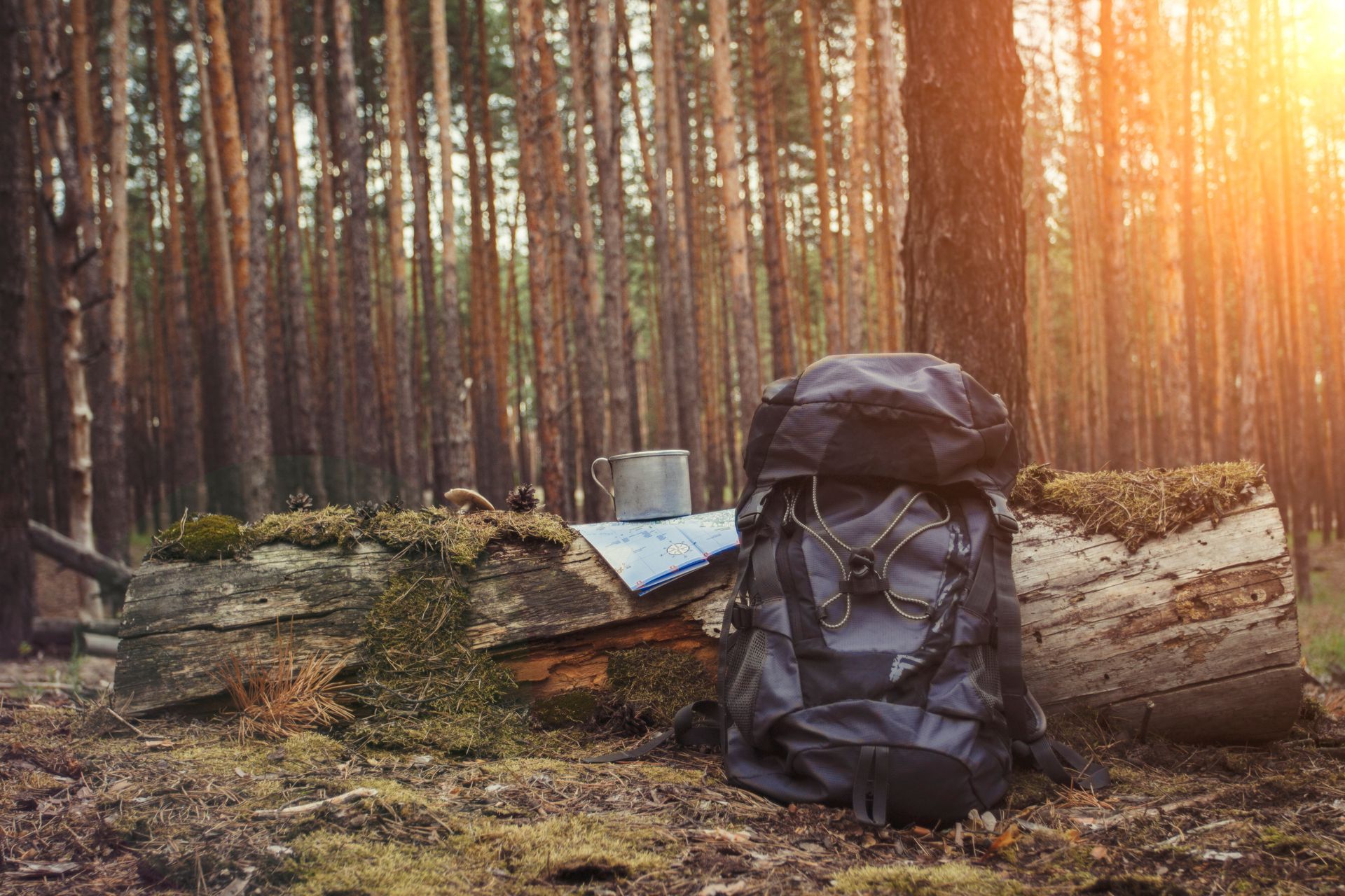 A backpack , boots , pots and pans are sitting on a wooden table.