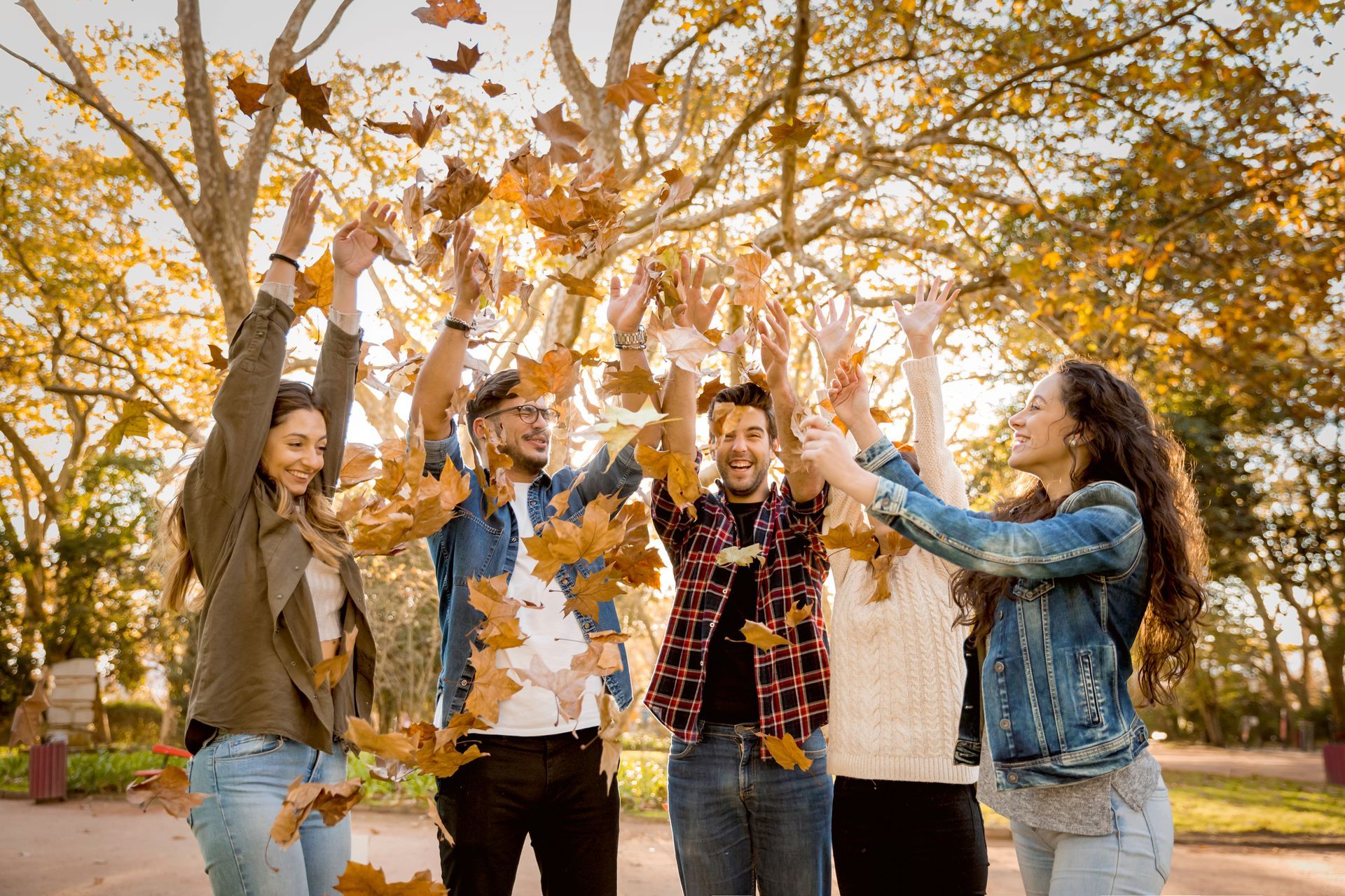 A group of young people are throwing leaves in the air in a park.