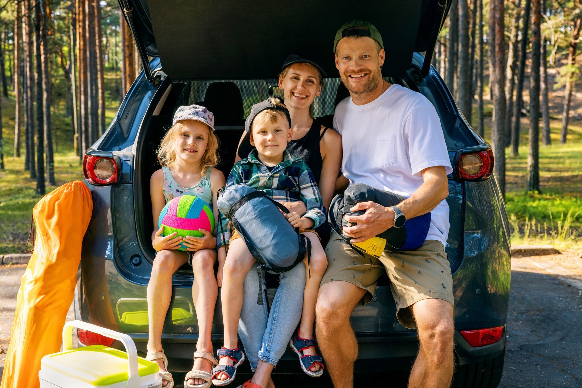 A family is sitting in the back of a car with camping gear.