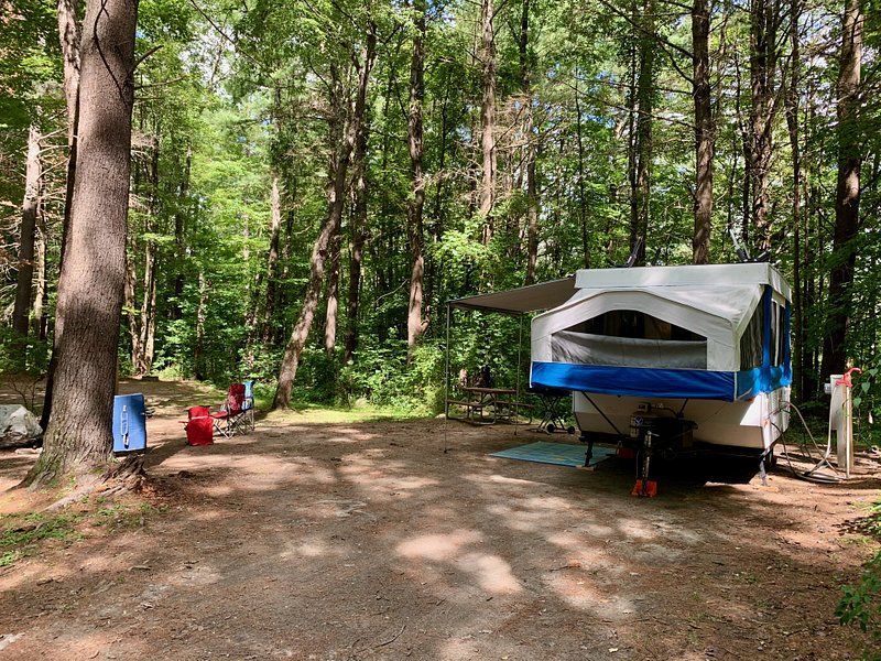 a rv is parked in the woods next to a picnic table .