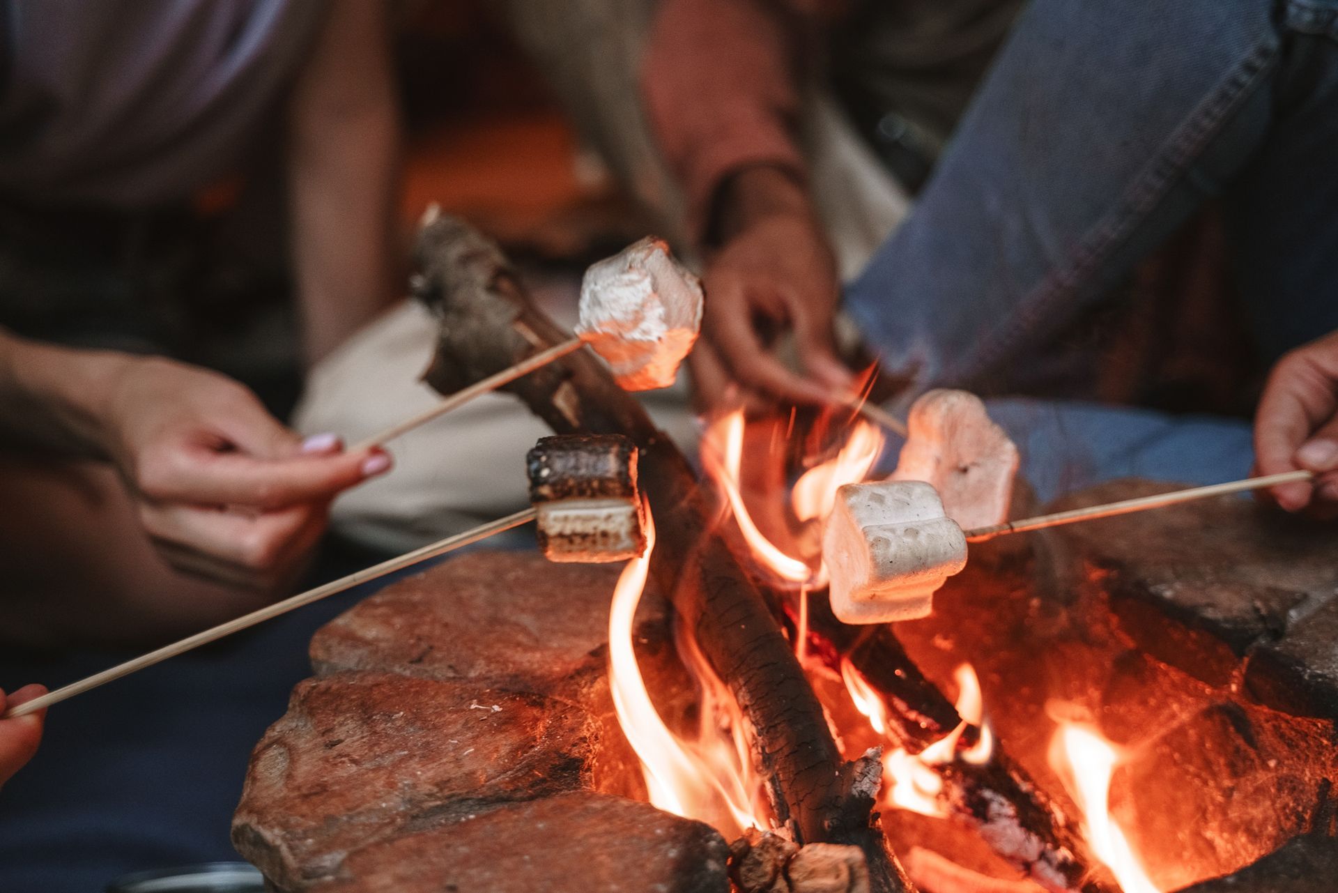 a group of people are roasting marshmallows over a fire pit .