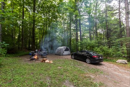 a car is parked in front of a tent in the woods .