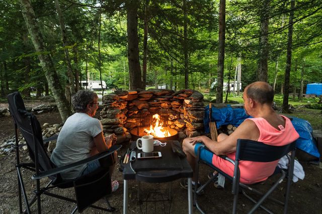 two people are sitting around a fire pit in the woods .