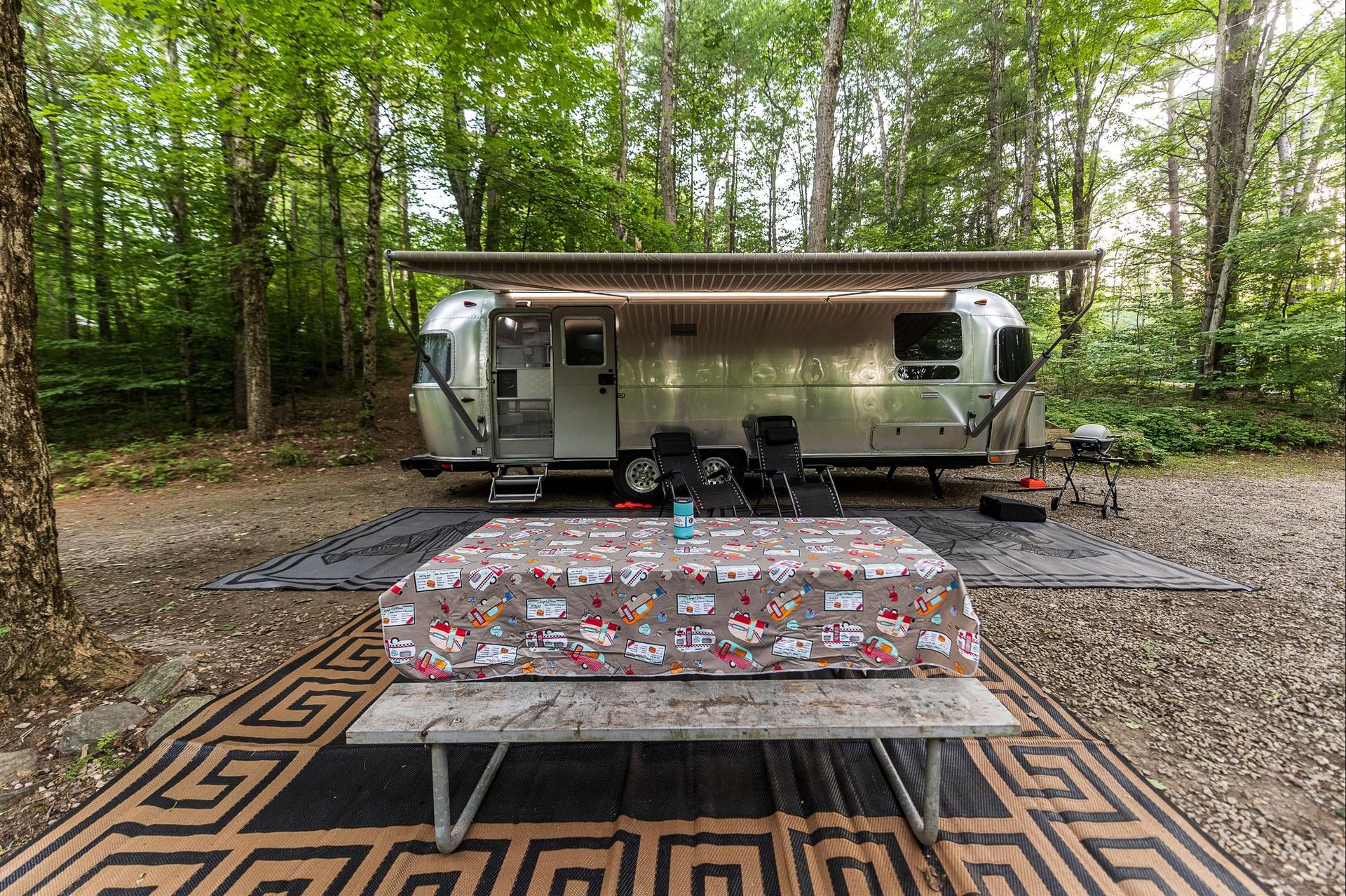 a rv is parked in the woods next to a picnic table .
