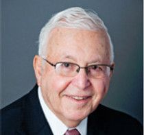 An older man wearing glasses and a suit and tie is smiling for the camera.