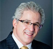 A man wearing glasses and a suit and tie is smiling for the camera.