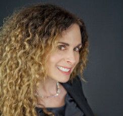 A woman with curly hair is smiling and wearing a black jacket.