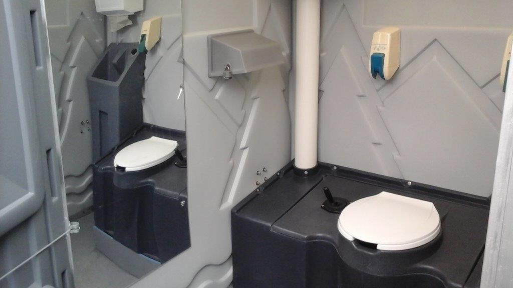 A portable toilet with two toilets and a hand sanitizer dispenser.