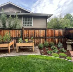 Backyard garden with wooden fence, raised beds, stone path, and birdbath.