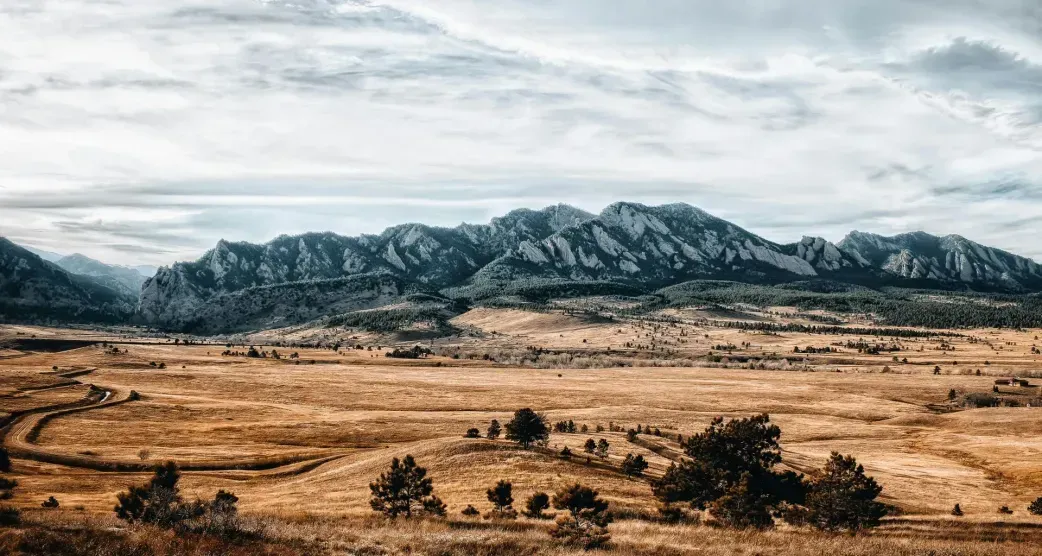 Mountains rise above a golden field under a cloudy sky.