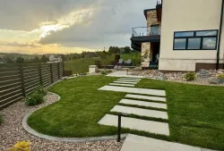 Grassy backyard with stepping stones leading to a modern house. Overcast sky with sunset glow.
