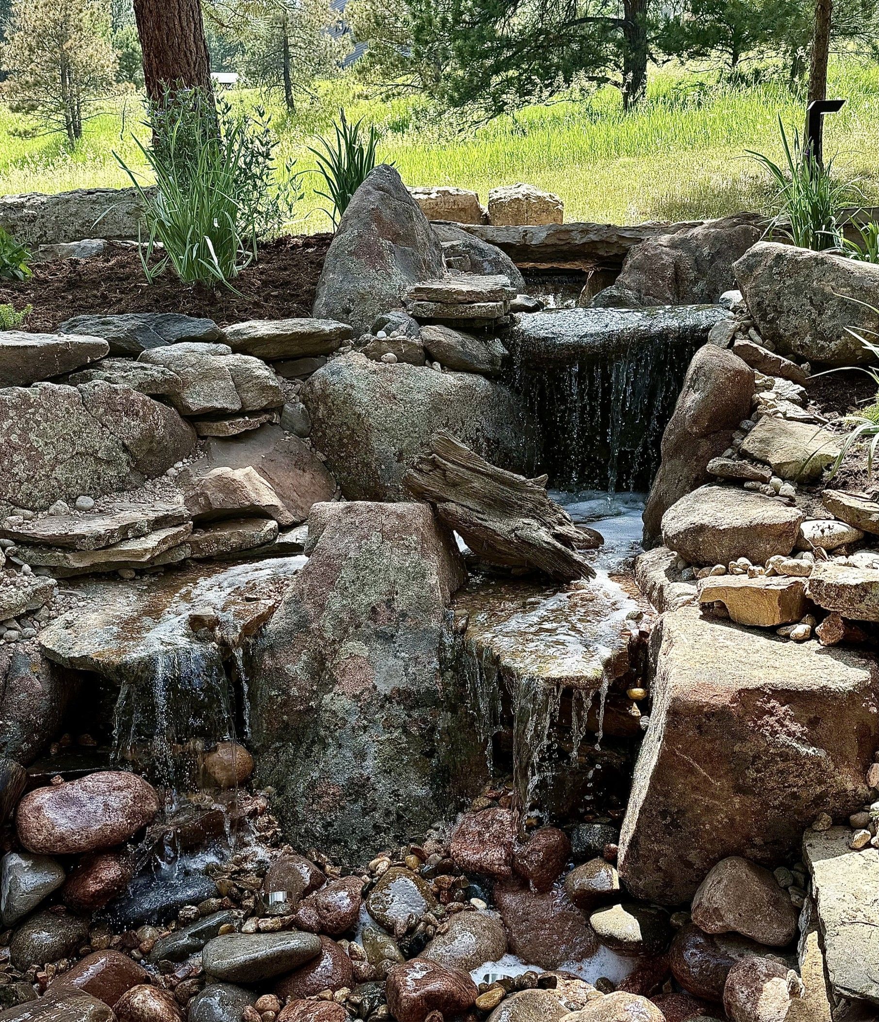 Water cascades over layered rocks in a small outdoor waterfall feature.