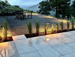 Patio with illuminated landscaping, gravel seating area, table, chairs, and mountain view.