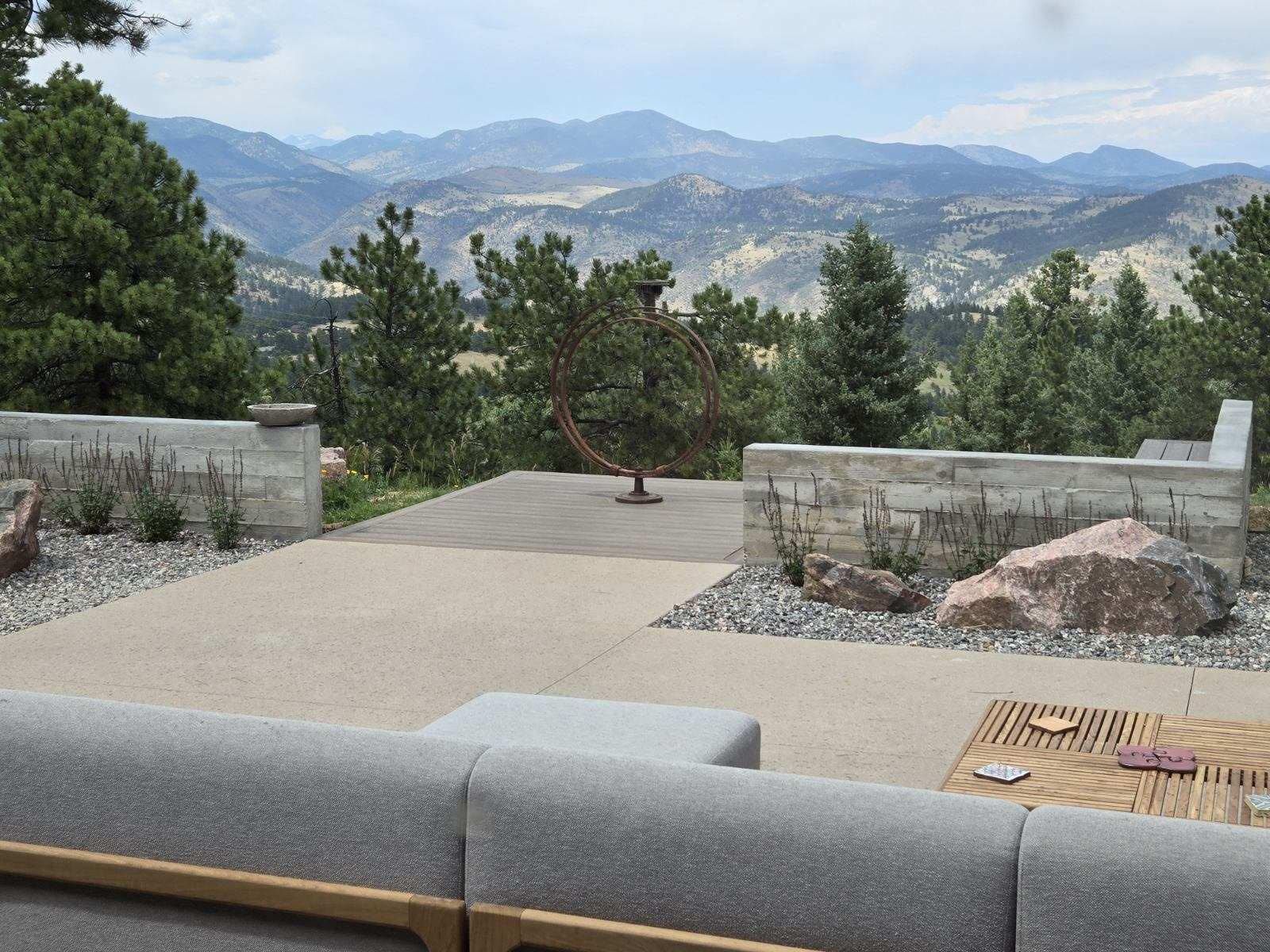 Patio overlooking mountain range, gray concrete walls, seating, small tree in the center.