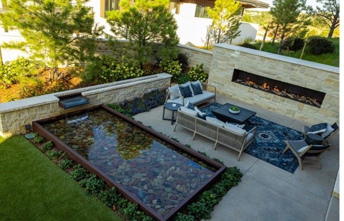 Outdoor patio with rectangular water feature, seating area, fireplace, and surrounding landscaping.