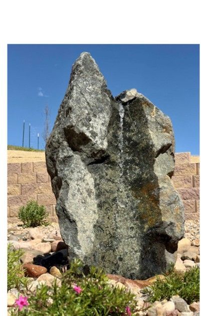 Water fountain made of a large, gray rock, water trickling down its side, in a rock garden.