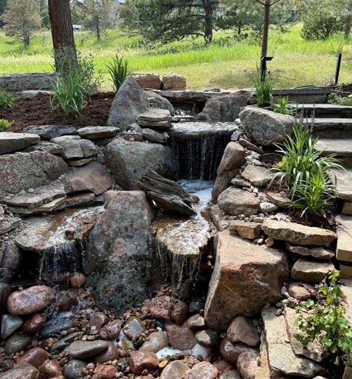 A cascading waterfall flows over stacked rocks in a landscaped garden.