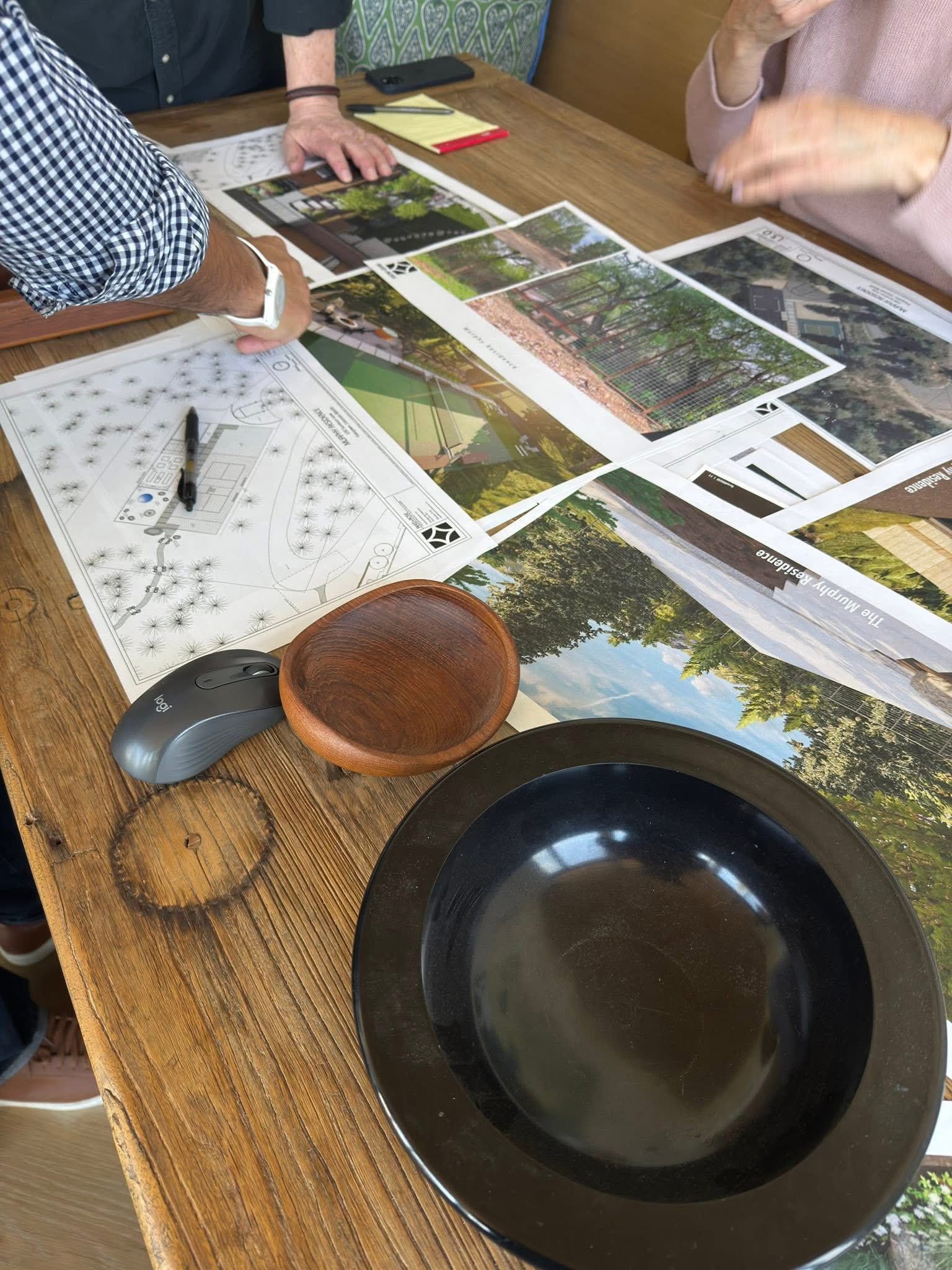People at a table looking at printed images, with a mouse, bowls, and pen present.