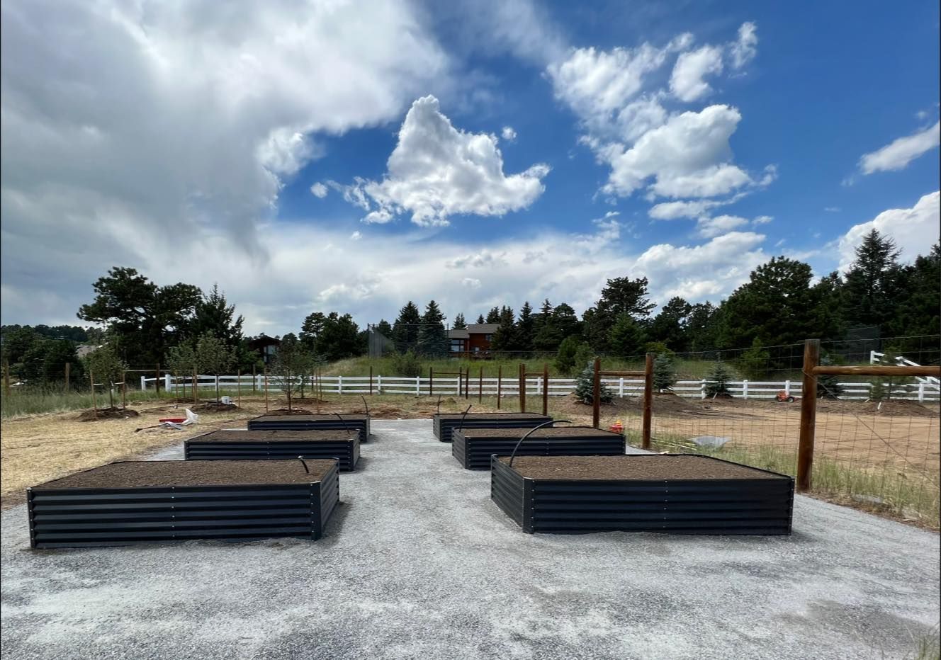 Outdoor garden beds filled with soil, set on a gravel path under a cloudy sky.