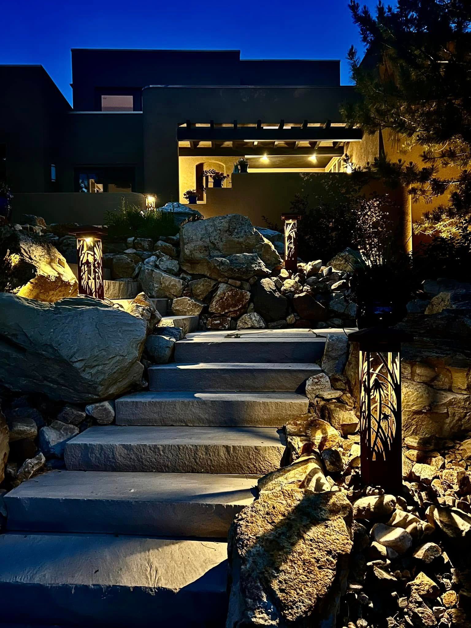 Stone steps lit at night lead up to a modern house. Decorative lights line the path.