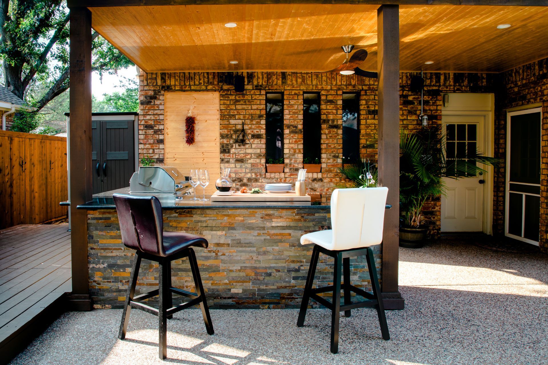 Outdoor bar with brick facade, granite countertop, bar stools, and wooden ceiling.