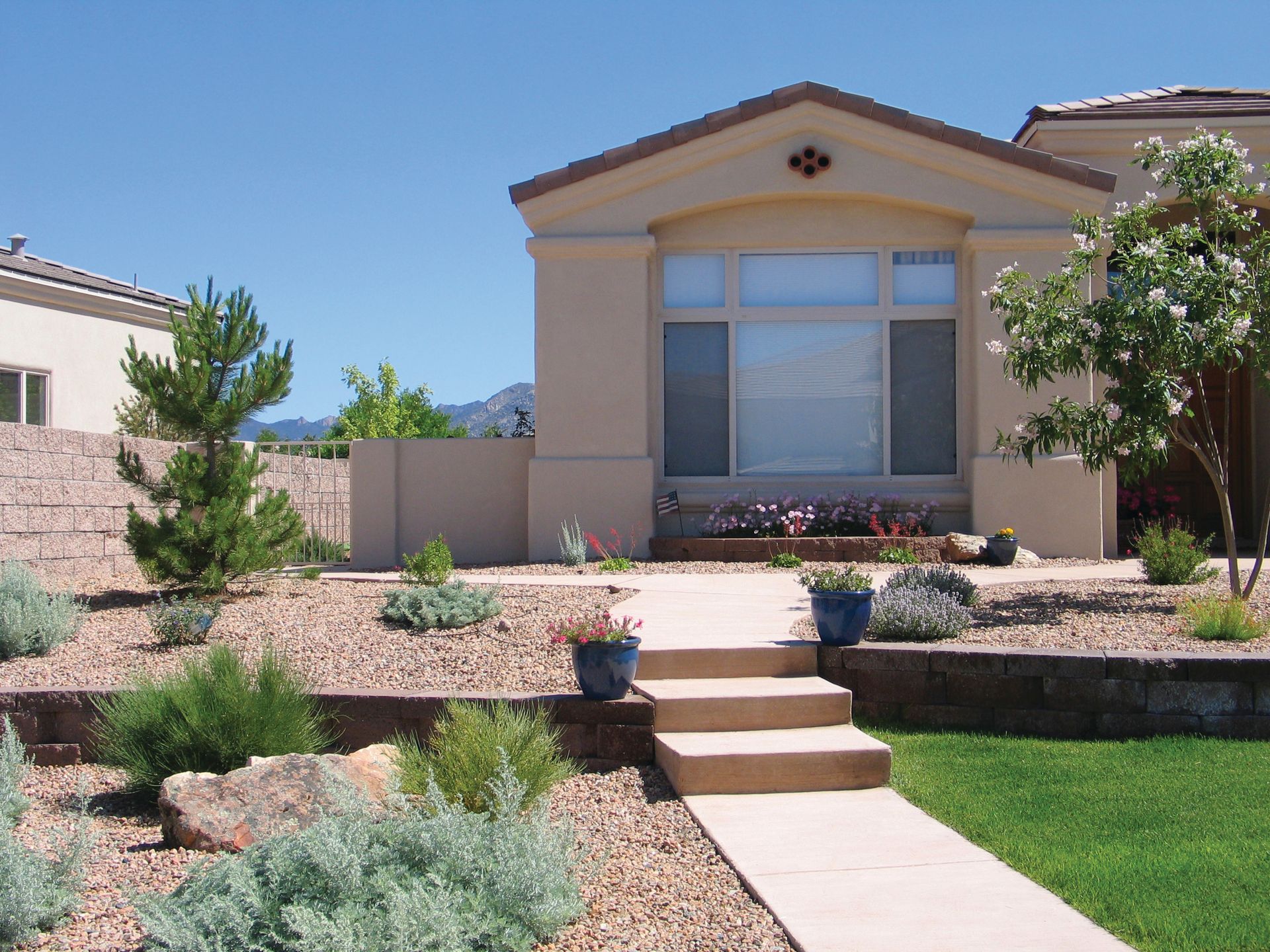 Tan stucco house with rock garden, concrete path, and blue pots.