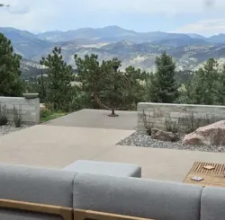 Patio with stone walls, rock landscaping, and mountain view. Gray couch in foreground.