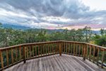 Wooden deck overlooking a forested mountain landscape under a cloudy sky.