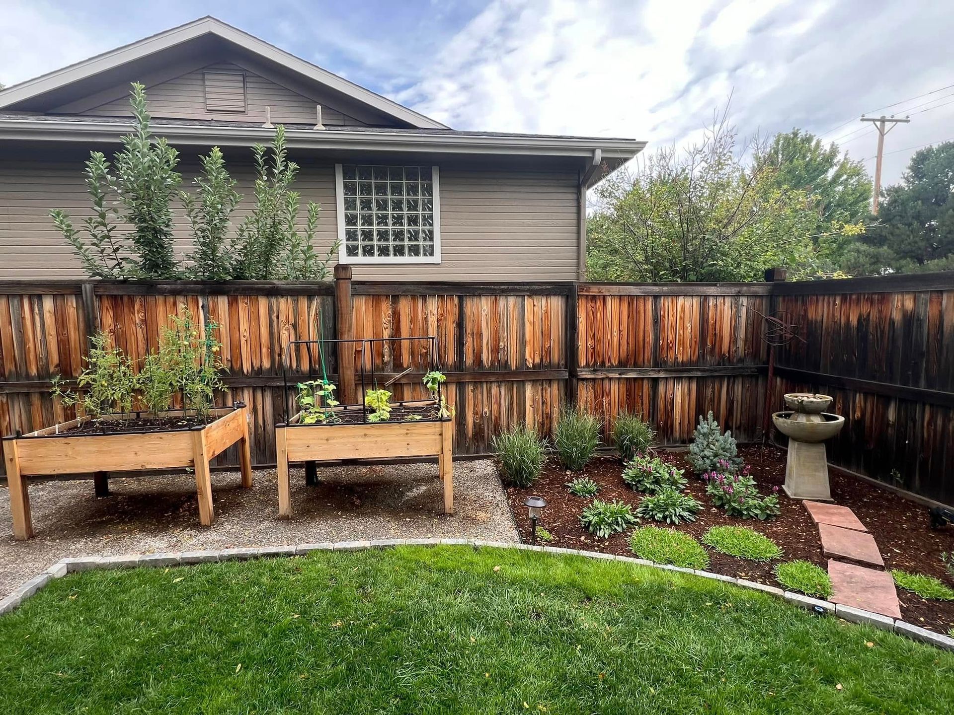 Backyard garden with wooden fence, raised beds, stone path, and birdbath.