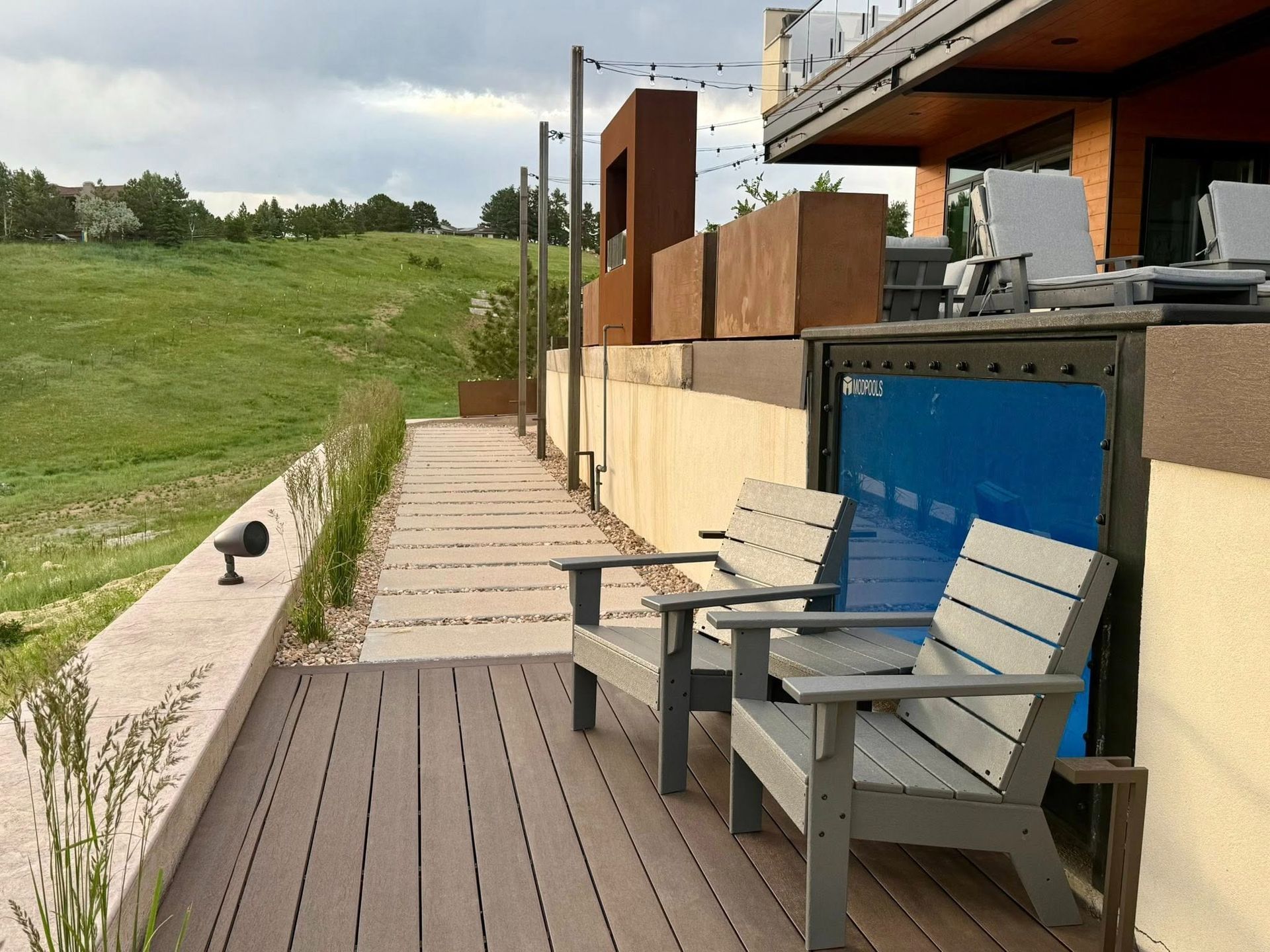Outdoor deck with two gray chairs, overlooking a grassy hill.