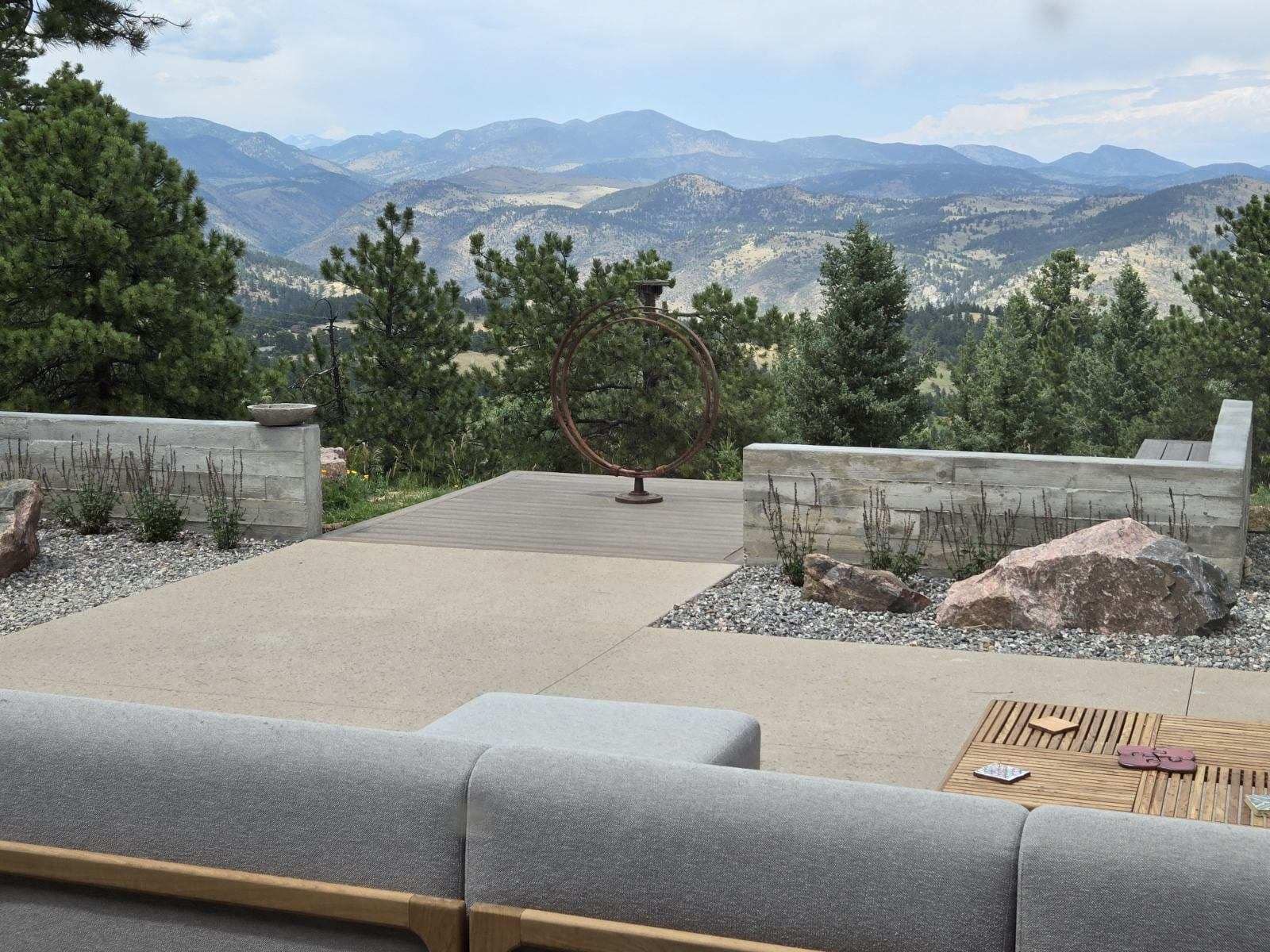 Patio with stone walls, rock landscaping, and mountain view. Gray couch in foreground.