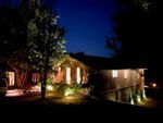 Night-lit wooden building, surrounded by trees. Warm lights illuminate the facade and surrounding foliage