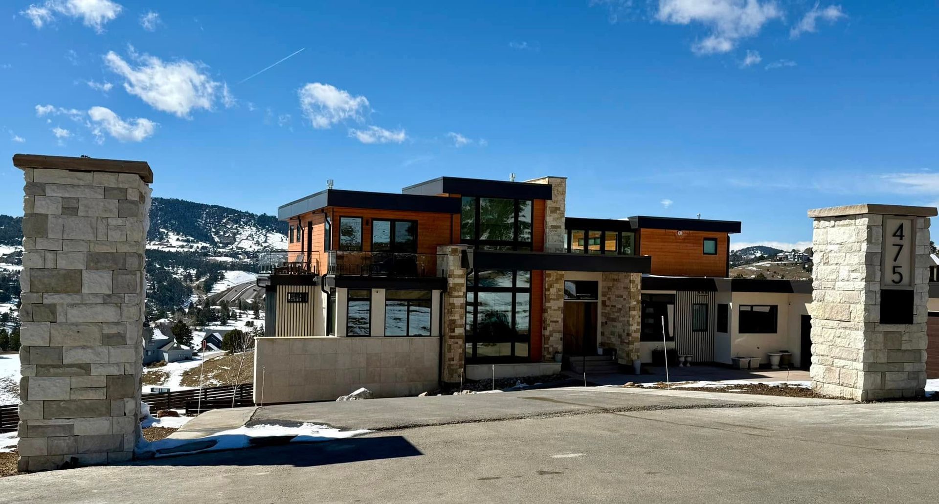 Modern house with stone pillars and a mountain backdrop under a blue sky.