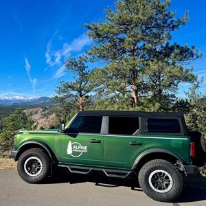 Green Ford Bronco on a scenic mountain road with a sunny blue sky.