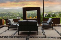 Outdoor seating area with fireplace, overlooking a valley at sunset.
