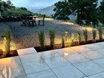 Outdoor patio with illuminated plants, gravel area, and mountain view.