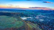 Panoramic view of a city nestled in a valley, framed by hills under a dusky sky.