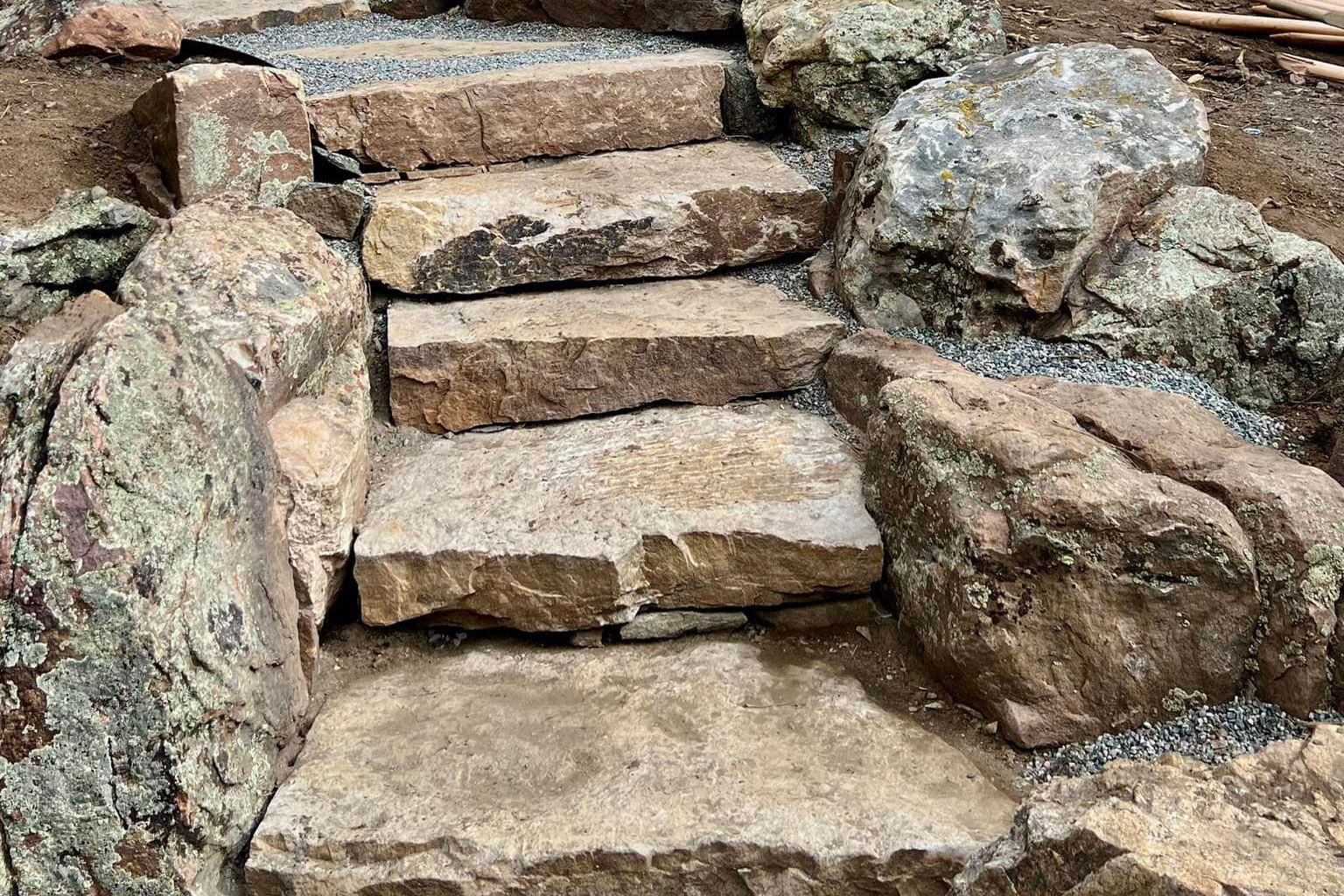 Stone steps built into a hillside, surrounded by large rocks and gravel.