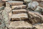 Stone steps leading upwards, built into a rocky hillside. Brown and gray tones.