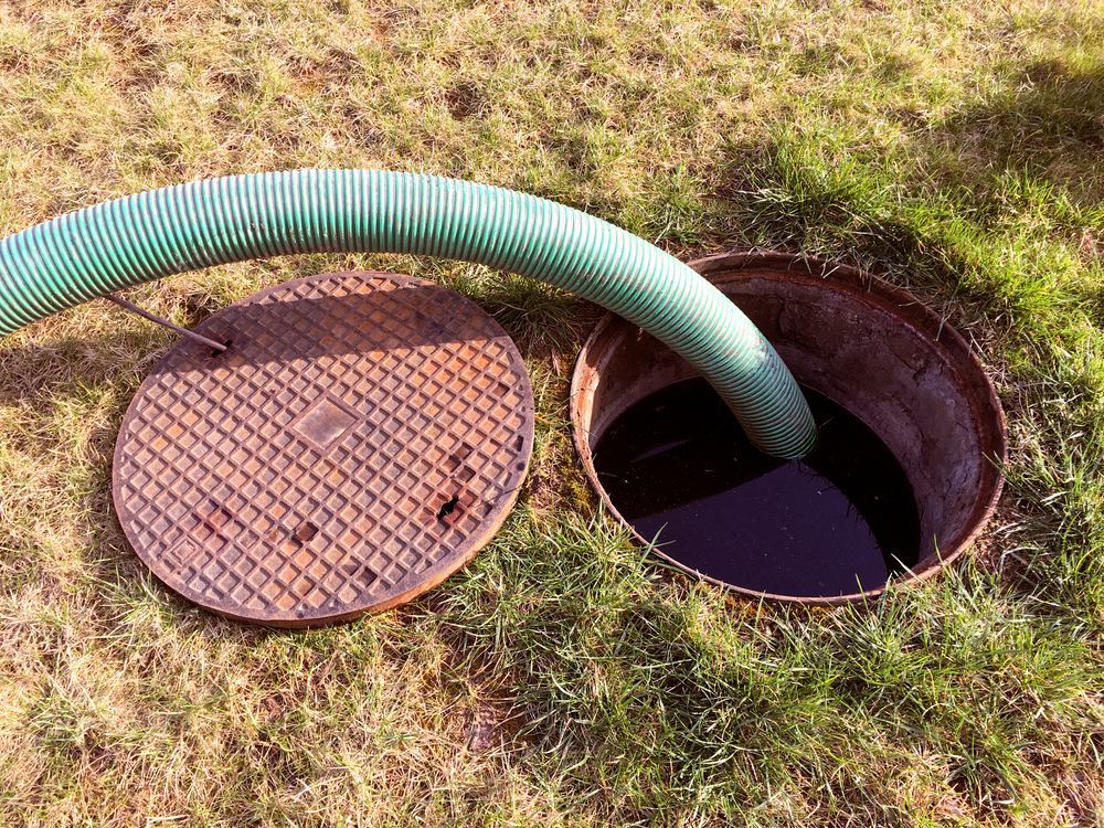 Green Hose Feeding Into an Open Manhole on Grassy Ground — Tamworth Septic & Liquid Waste in Wallabadah, NSW