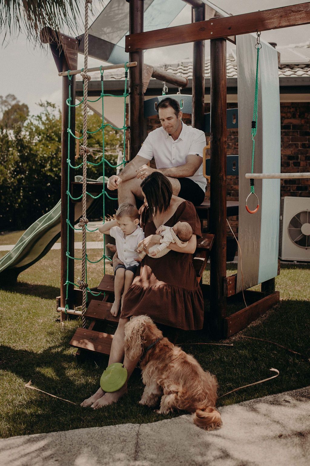 Family of five, plus dog, pose on a wooden play structure in a backyard.