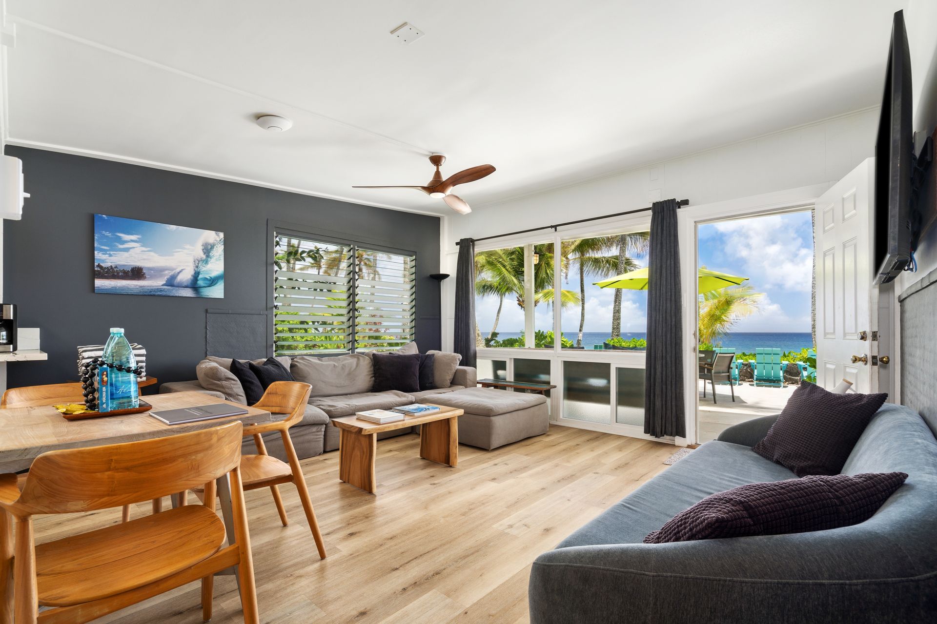 Bright living room with ocean view. Gray couches, wooden furniture, and a dark blue accent wall.