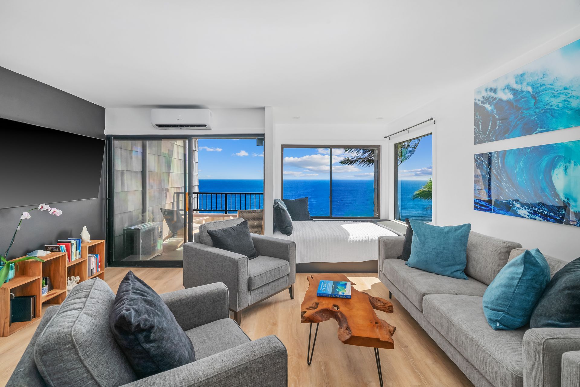 Living room with ocean view, gray couches, blue pillows, wooden coffee table, and artwork.