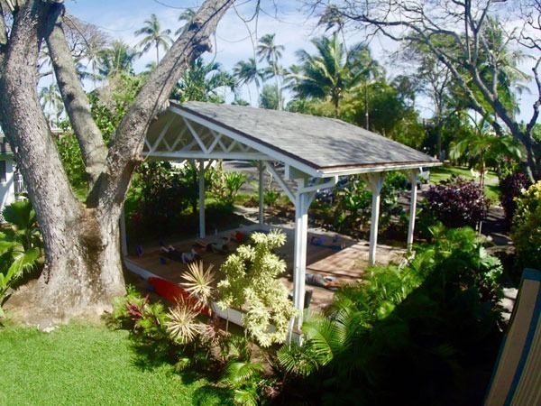 White gazebo with roof in a lush green tropical garden.