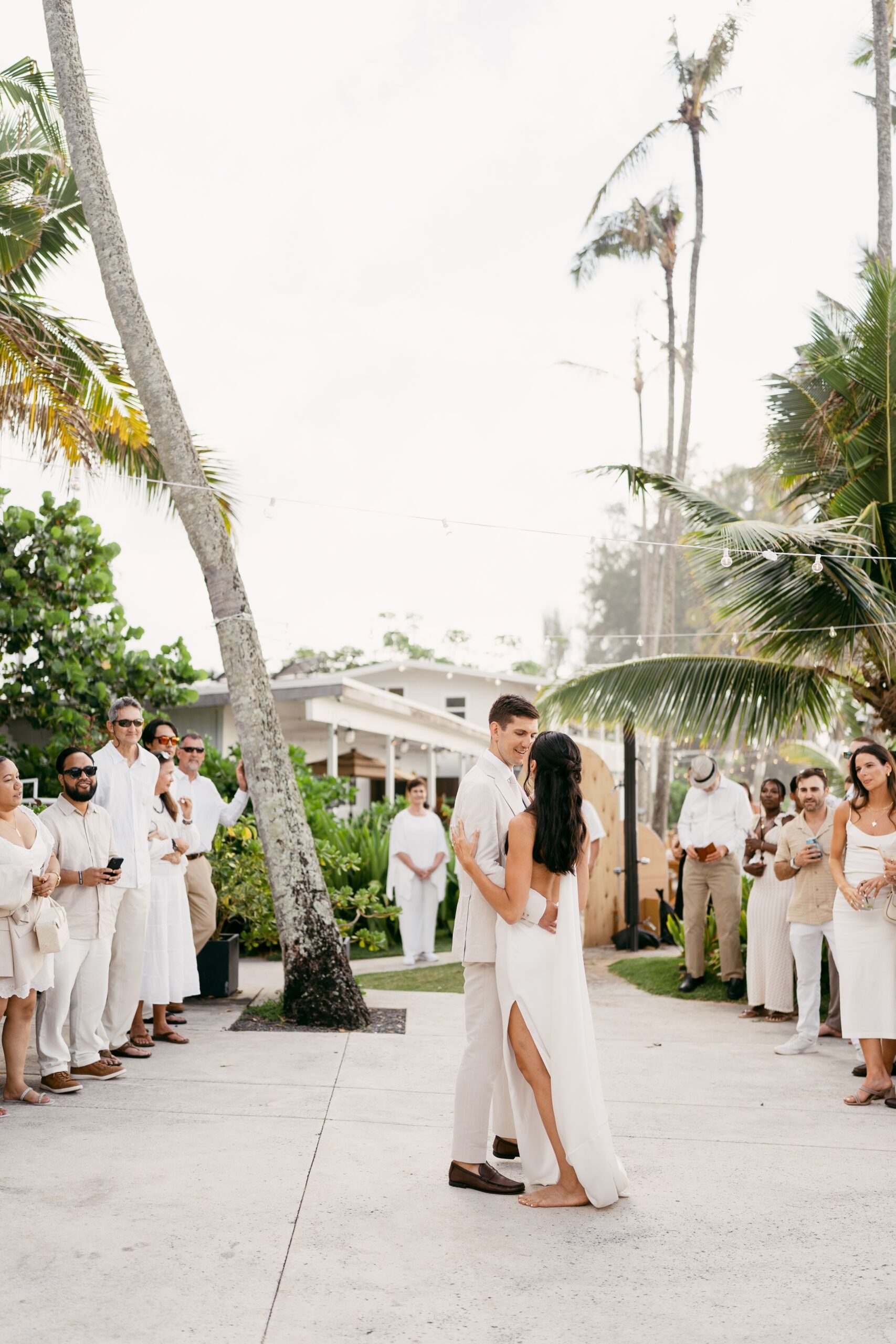 Bride and groom dance, tropical setting; guests in white.