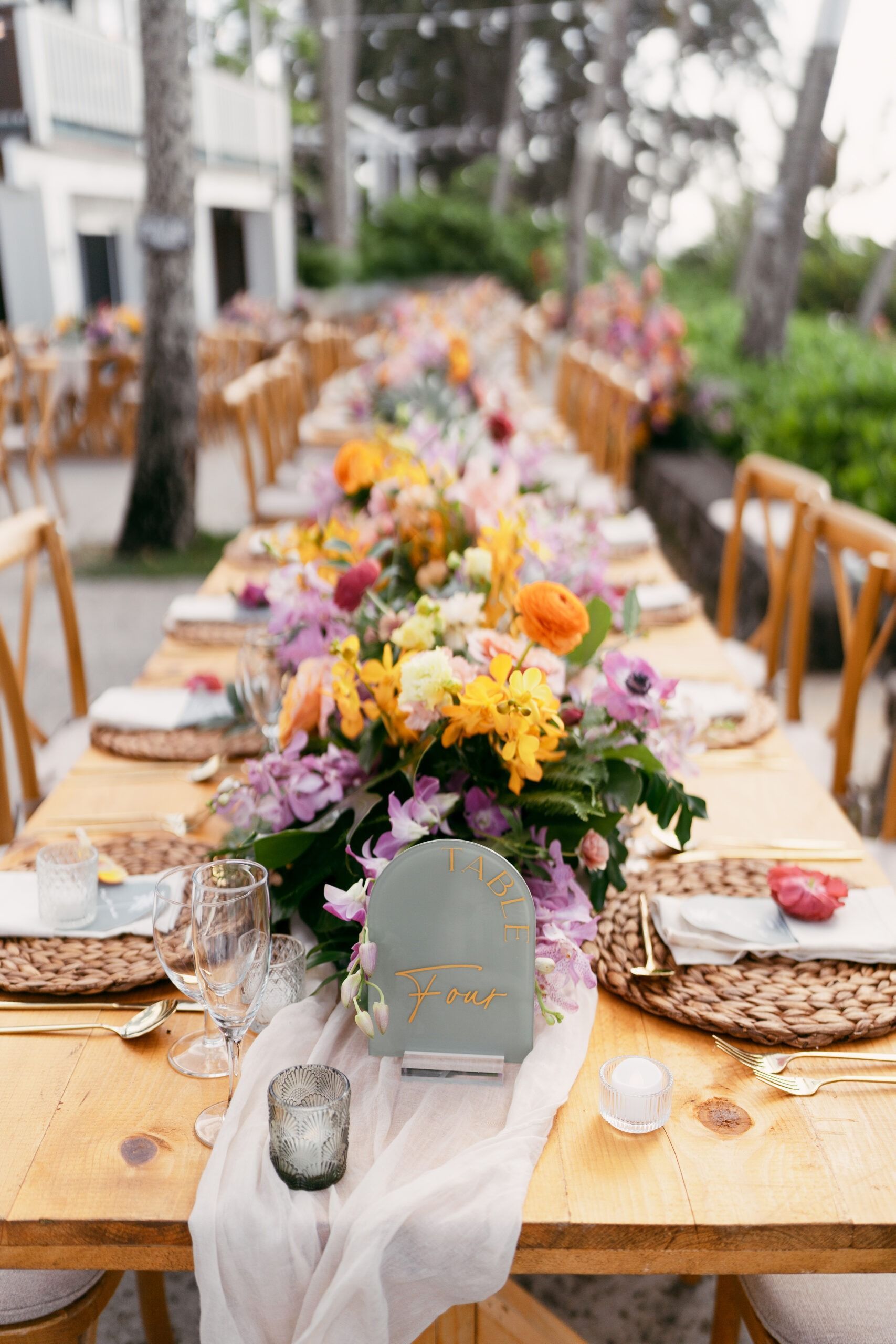 Long wooden table set for a celebration, featuring floral centerpieces, place settings, and a guest name card.